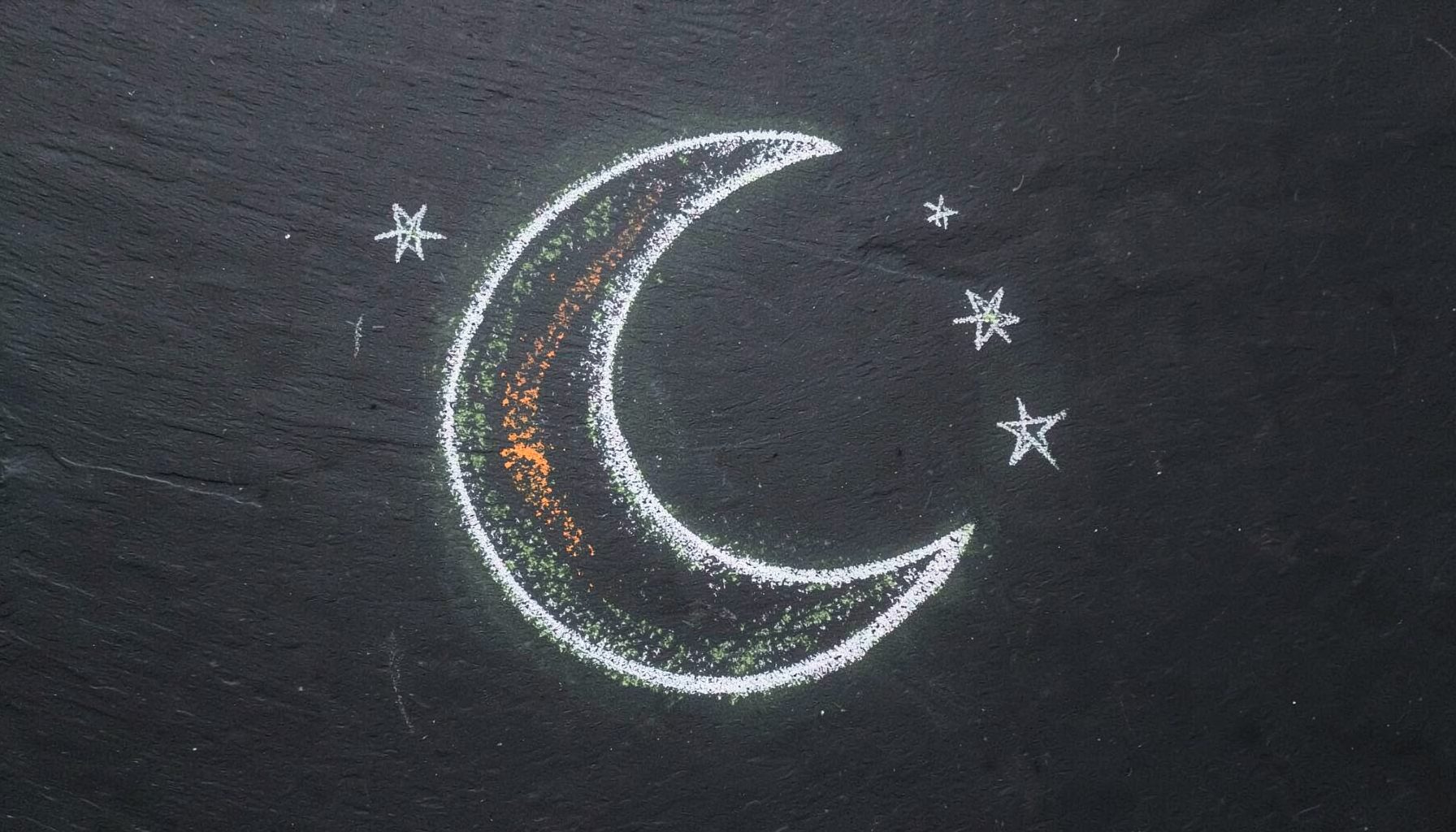 A chalk drawing on a dark slate board of a crescent moon surrounded by a few small stars, sketched in soft white chalk lines