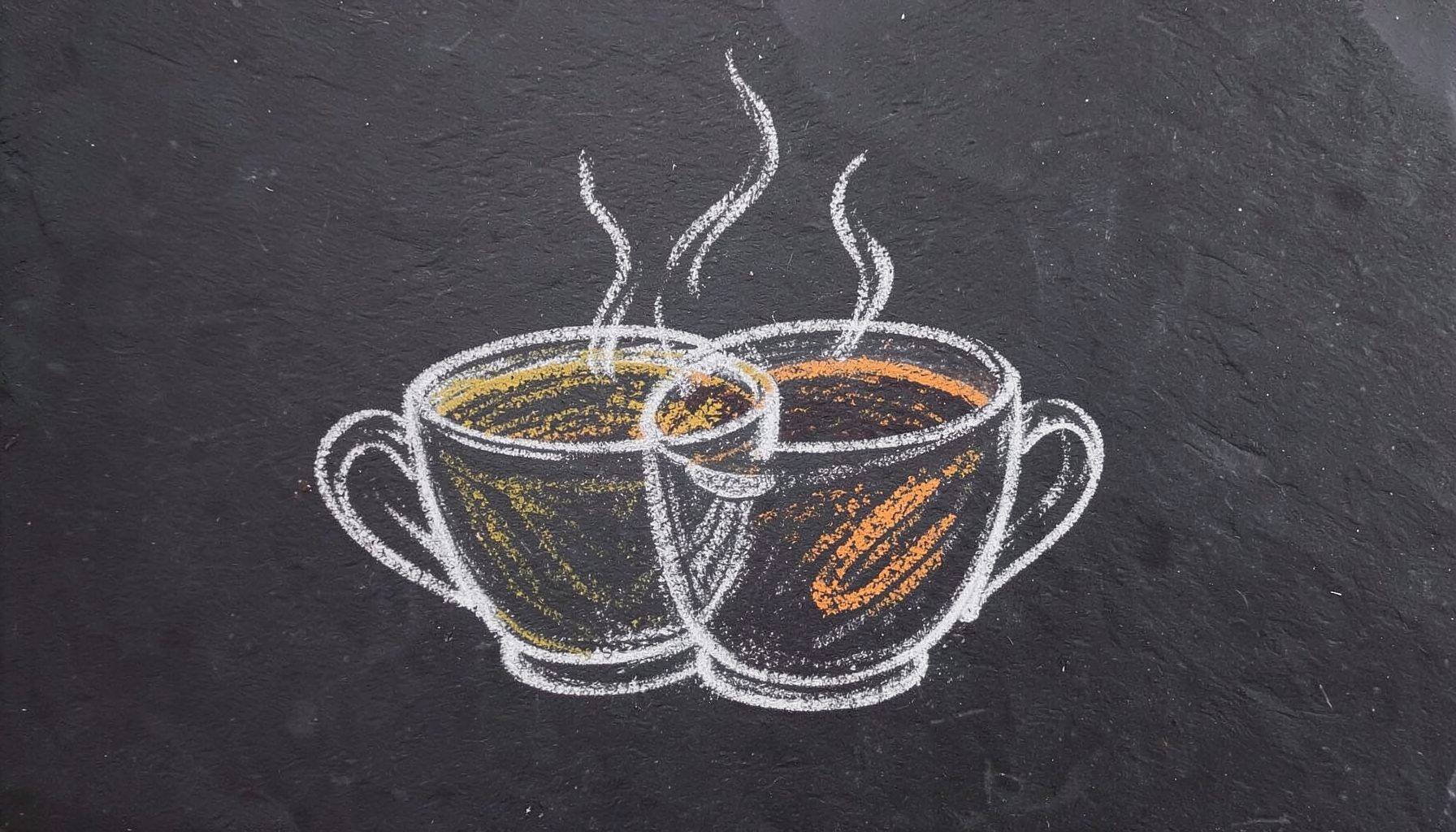 A chalk drawing on a dark slate board of two overlapping coffee cups with gentle curling steam lines, drawn in soft white chalk